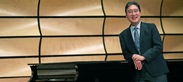 Dean Michael Kim standing at a piano in von Kuster Hall, Music Building
