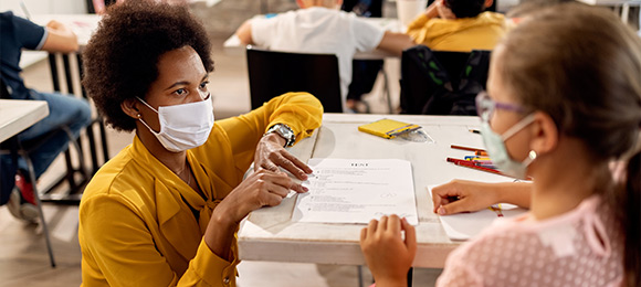 A teacher talks to a student while both are wearing masks.