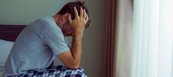 A man holding his head in his hands while sitting on a bed.