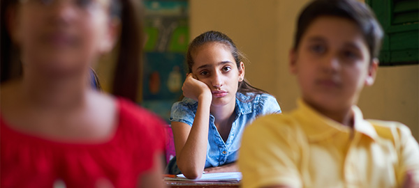 Students looking towards the front of the classroom. One student looks bored with her head in the palm of her hands.