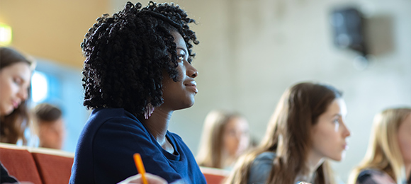 Students sitting in a lecture hall while listening to a lecture.