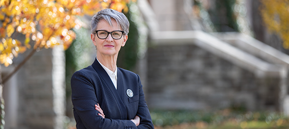 A photo of Lisa Henderson in a navy blazer standing outside on campus in the fall.