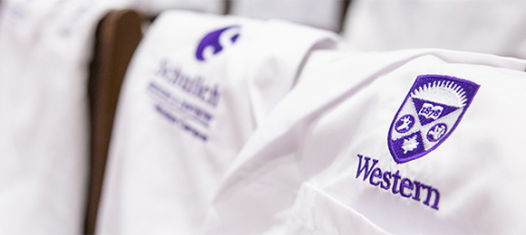 A white doctors coat draped over a chair, with the camera focus on the embroidered Western and Schulich logos