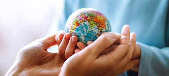 Child's hands holding a small globe with adult hands supporting underneath