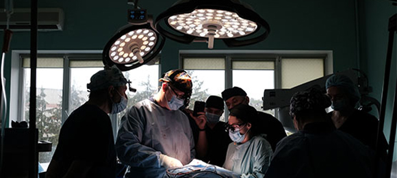 Team of surgeons working on a patient. The image is mostly dark with the surgical lights illuminating the two surgeons in the centre of the photo.
