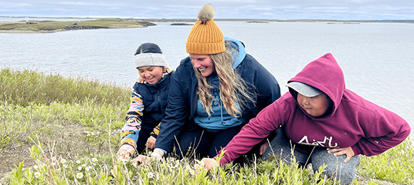 Paige Driscoll and two students examine the ground near a lake. 